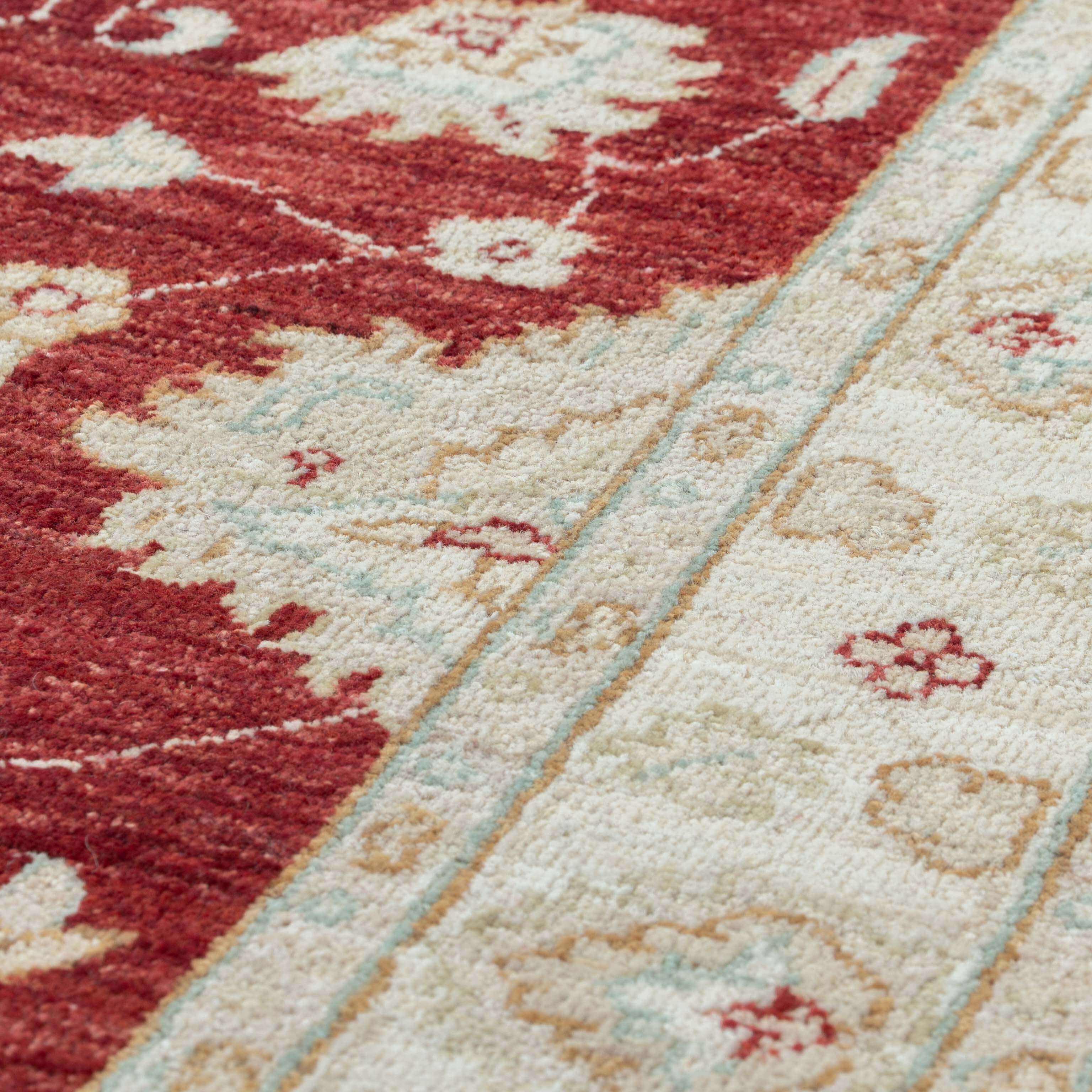 Close-up of a patterned area rug with a deep red field, cream sections, and a decorative border in pale blue and beige tones.