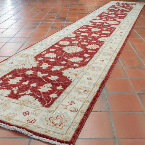 A long runner rug with a traditional floral pattern in red and cream, laid out on a terracotta tiled floor.