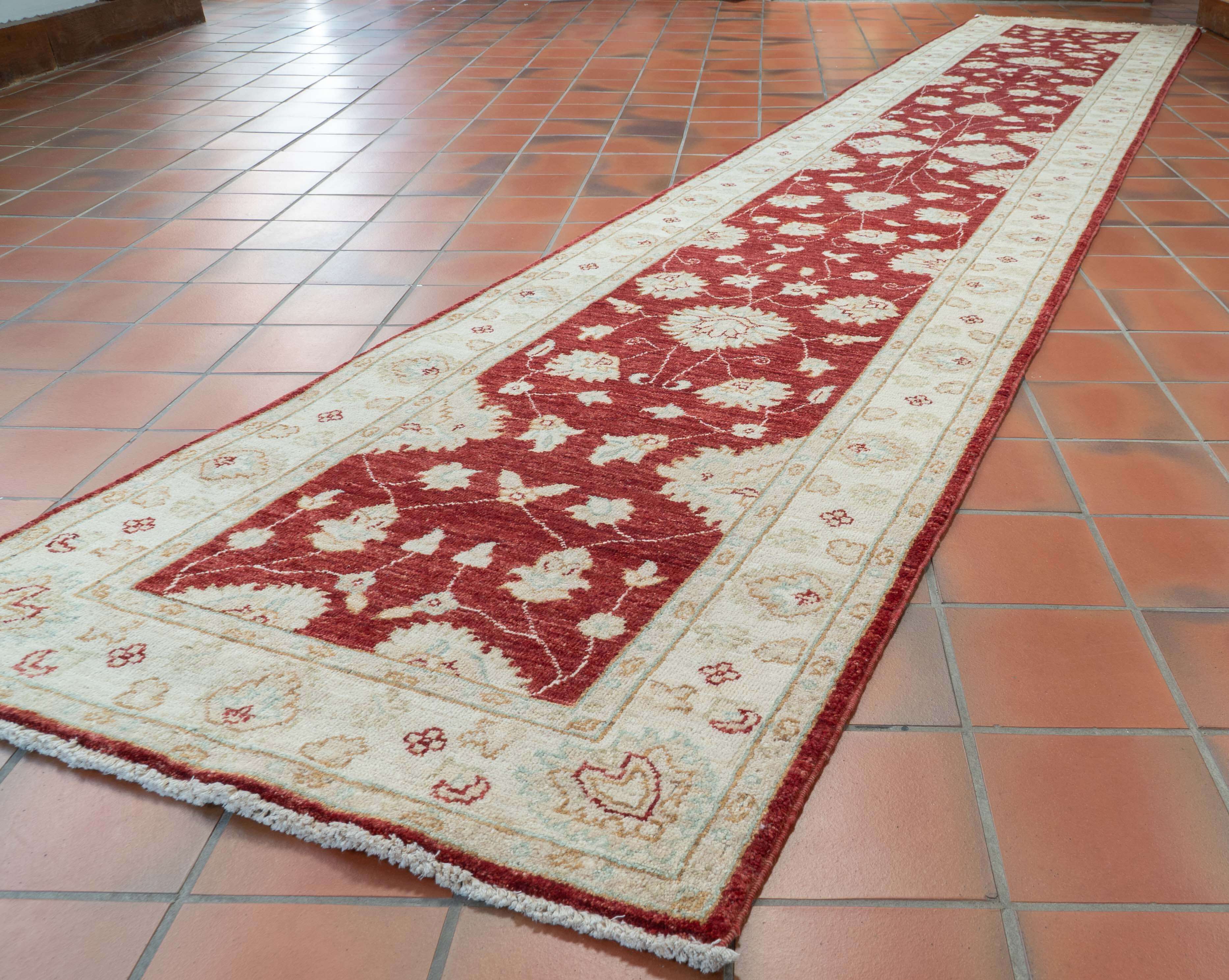 A long runner rug with a traditional floral pattern in red and cream, laid out on a terracotta tiled floor.